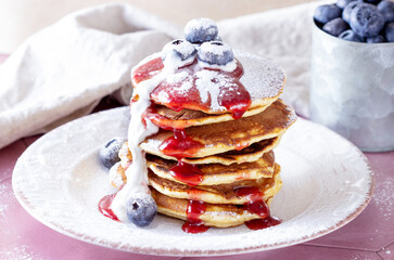 pancakes with jam, sour cream and blueberries sprinkled with powdered sugar. Pancakes for breakfast are stacked