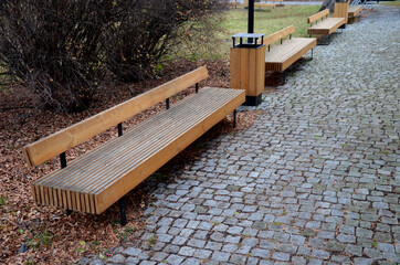wooden long bench, where the seating area is formed by rows of vertical planks and a backrest. notches are possible on the edges of the bench for inserting a bicycle tire. park with perennials 