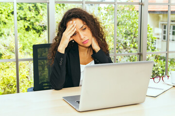 Businesswoman sits at her desk looking after her laptop, stressed and overwhelmed by work and...