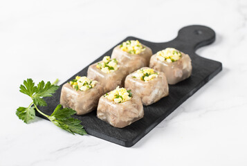 Jelly made from thickened meat broth from cooking, with pieces of pork in the form of small portions with finely chopped egg and parsley on a serving board on a white background