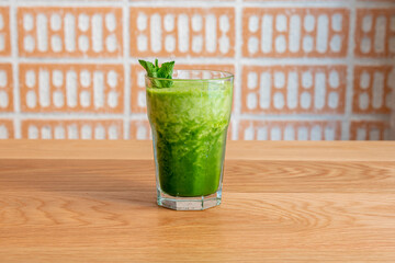 Detox smoothie with spinach and kiwi and topped with some mint leaves on wooden table