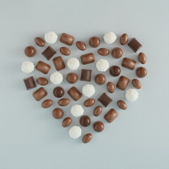 Creative love arrangement made of chocolate pralines that form a heart shape on a gray background....