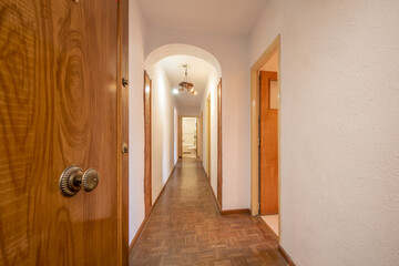 Wooden entrance door to a home with a long corridor flanked by pine wood doors