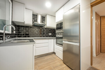 Fototapeta premium kitchen with white cabinets white brick wall black tiles and aluminum appliances leading to an office with venetian cabinets