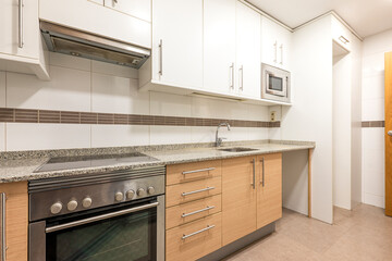 Fototapeta premium Kitchen with white cabinets, black and white granite countertops, white tiles and brown trim paired with stainless steel appliances