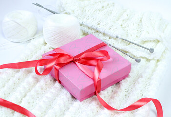 DIY gifts. Pink gift box tied with a pink ribbon on a knitted white sweater, close-up.