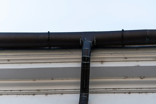Part of a house exterior white wall with brown  rain gutter system with a downspout.