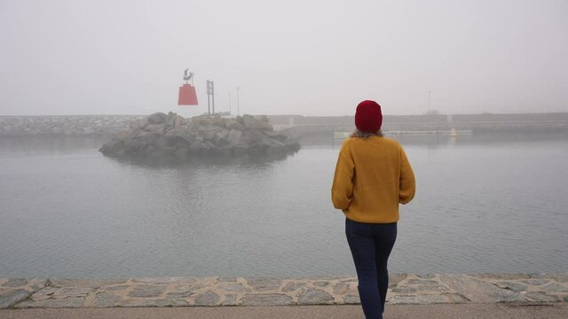 Woman approaches the sea and enjoys the views of the lighthouse and sea on a sad and cloudy day.