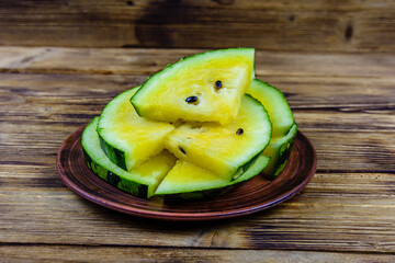 Plate with sliced yellow watermelon on a wooden table