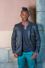 Dressing in a black blazer, green pants, a young black guy with mohawk hair is standing against the...