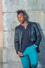 Obraz premium Dressing in a black blazer, green pants, a young black guy with mohawk hair is standing against the wall, looking down into deeply thinking..