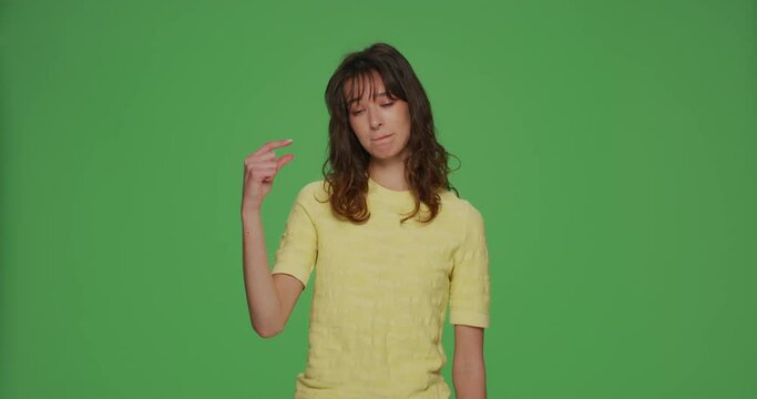 Upset young girl look at hand showing with pity little size gesture, shrug and sigh on chromakey green studio background