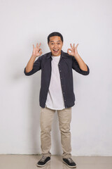 Portrait of excited handsome asian man in shirt smiling and showing ok sign with two hands at camera isolated on white background 