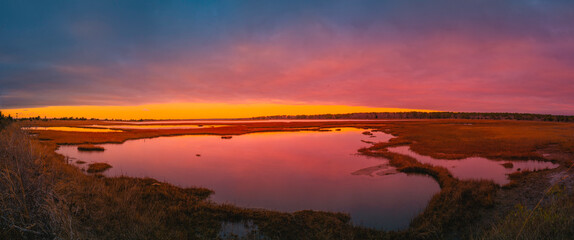 Fototapeta na wymiar Sunrise panoramic seascape over the marsh pond in Mashpee on South Cape Beach, Massachusetts. Pink and blue western sky and water reflections at cloudy dawn.