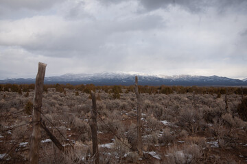 An old fence propped up along the highway , in the background snowy mountains peak through the clouds. 