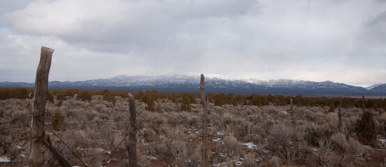 An old fence propped up along the highway , in the background snowy mountains peak through the clouds. 