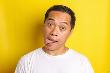 Close-up portrait of asian man with mocking expression, reproaching, and sticking out tongue isolated on yellow background