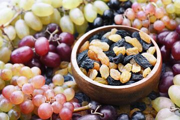 Naklejka na ściany i meble Dried yellow and black raisins in bowl on fresh ripe grape background, selective focus, shallow DOF