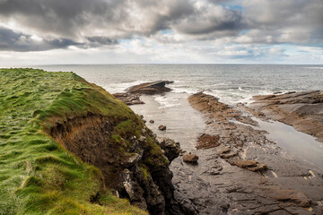 Green grass fields by the ocean and rough stone coastline, low cloudy sky. West coast of Ireland. Irish landscape. Nobody.