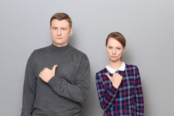 Portrait of serious man and woman  pointing at each other with thumbs