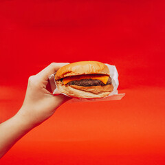 Hamburguesa deliciosa comida rápida sostenida con la mano de mujer con fondo rojo
