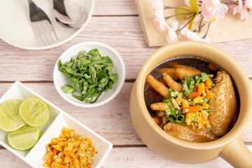 Homemade Spicy Chicken feet and Wings serving in clay pot on wooden table. Famous Thai local food made from chicken feet, wings, spices, herbs, lime juice, chili and another ingredients.