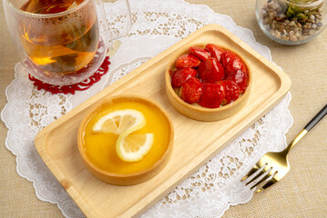 Fresh baked Lemon Tart topping with lemon sliced and Fresh Strawberries Tart topping with strawberries sliced, serving on wooden plate with hot tea, good for sweet teatime