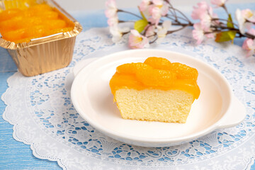 A Piece of Orange Sponge Cake topping with Sliced Orange, made from organic fresh orange juice, served on white plate on white lace placemat