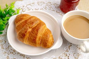Freshly baked tasty croissant with strawberry jam served with hot coffee on white lace placemat