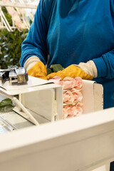 hand of a person protected with gloves while working packing a bouquet of roses with cardboard, sending fresh flowers