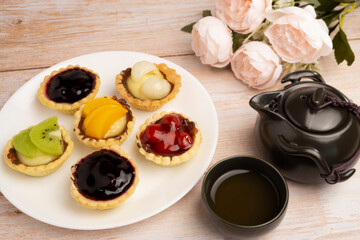 Homemade Fruits tarts, Sweet desserts topping with fresh kiwi, blueberries, peach, longan, raspberries in syrup, served with hot herbal tea on wooden table