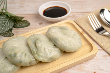 Steamed Chives Dumplings or Leek Stuffed Dough, steamed dumpling stuffed with sliced garlic chives serving on wooden tray with special soy sauce. It is called 