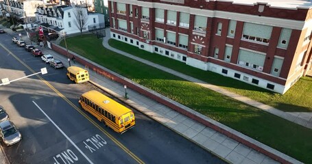 School bus and students at public school building. Exterior aerial establishing shot of urban city American educational system.