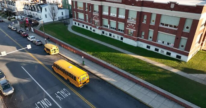 School bus and students at public school building. Exterior aerial establishing shot of urban city American educational system.