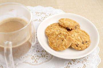 Homemade Freshly Baked Oat Cookies served on white plate with hot coffee on white lace placemat, good for breakfast or snack.