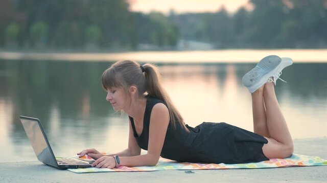 Young woman working behind laptop lying down in summer park outdoors