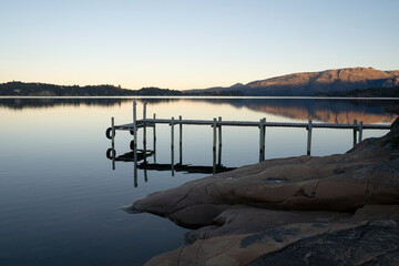 Magical view of the wooden dock in the placid lake at nightfall. The mountains, forest and blue sky...