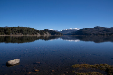 View of the lake in a sunny day. The forest, mountains and blue sky reflection in the water surface. 