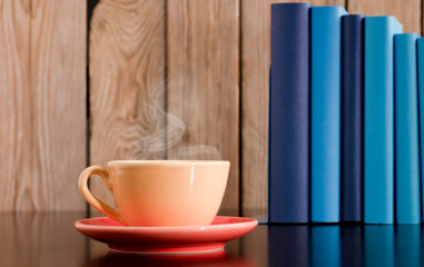 Yellow cup of coffee or tea with hot steam, on wooden table, with light blue and blue books. wood background