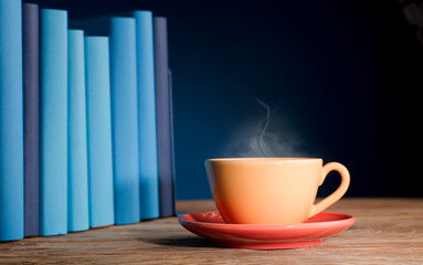 Yellow cup of coffee or tea with hot steam, on table wooden with light blue books and blue background.