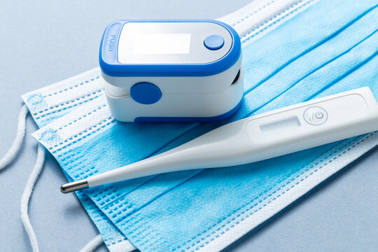 A digital thermometer next to an oximeter on top of some blue face masks