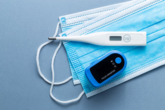 A digital thermometer next to an oximeter on top of some blue face masks