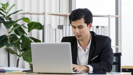 Millennial Asian male professional businessman in formal outfit sitting at work desk using typing notebook laptop computer browsing internet website reading documents check email in company office