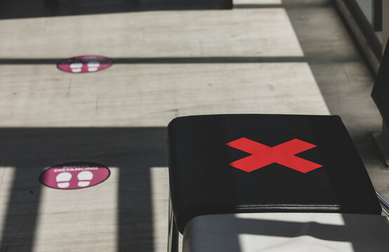 Close up light and shadow shot of red cross sticker marker warning symbol on waiting chair in office to keep space social distancing and footstep caution decal sign on floor in blurred background