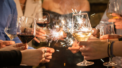 Close up on hands of group of people holding glasses of wine and sparkles while toasting and celebrating indoor focus on sparks birthday or new year celebration concept