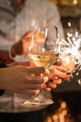 Close up on hands of group of people holding glasses of wine and sparkles while toasting and celebrating indoor focus on glass of wine birthday or new year celebration concept