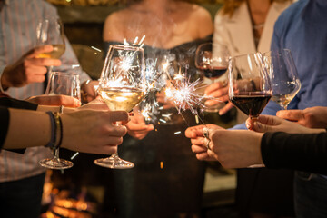 Close up on hands of group of people holding glasses of wine and sparkles while toasting and celebrating indoor focus on sparks birthday or new year celebration concept