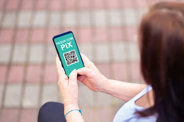 Woman holding Smartphone and making payment via PIX.  PIX is a new electronic payment system in...