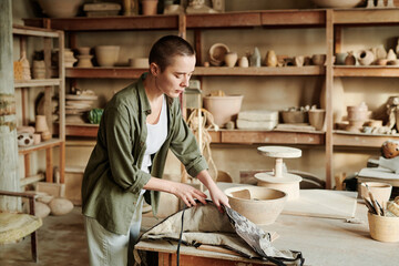 Craftswoman standing at her workplace and taking her apron, she preparing for her work in workshop