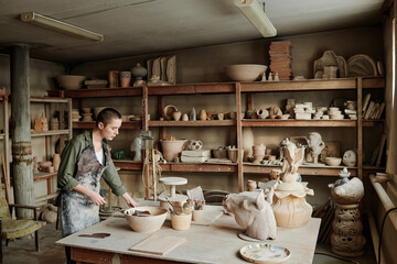 Young woman creating ceramic sculptures with clay at the table in workshop